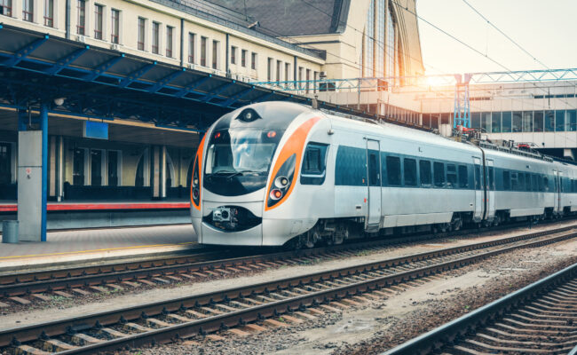 High speed train at the railway station at sunset in Europe. Modern intercity train on the railway platform. Industrial landscape with passenger train on railroad. Railway transportation. Locomotive